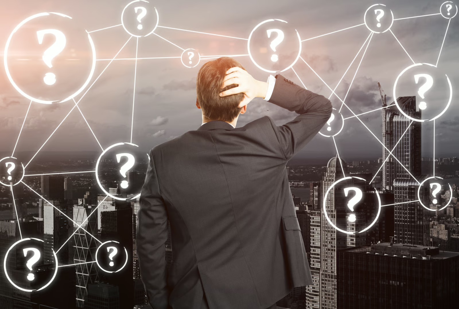 A businessman seen from behind scratches his head in confusion while looking out at a city skyline covered by a glowing white network of question marks.